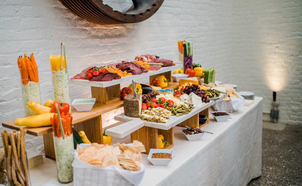 A buffet table with assorted vegetables, fruits, crackers, meats, and cheese displayed on wooden stands.