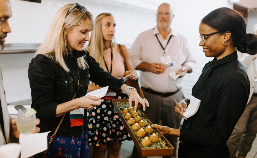 A server offers appetizers on a tray to a group of people at a social event.