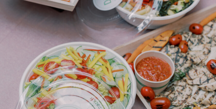 Catered salads, grilled veggies, dips, and salmon on platters, labeled "Dish Food & Events" on clear lids.