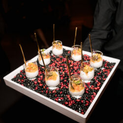 A tray with small parfait glasses on a bed of black and red beans, each with a gold spoon inside.