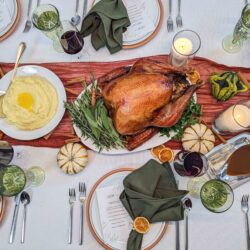 Roast turkey, mashed potatoes, drinks, and candles on a festive table set with green napkins and menus.
