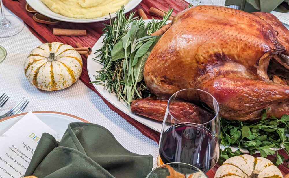 Roast turkey on greens, mashed potatoes, wine, and pumpkins on a festive dinner table set with green napkins.
