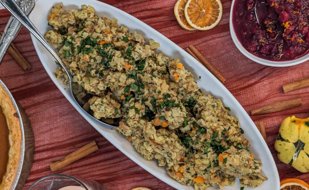 Oval dish of stuffing with herbs, cranberry sauce, pie, dried orange slices, candle, and wine on a table.